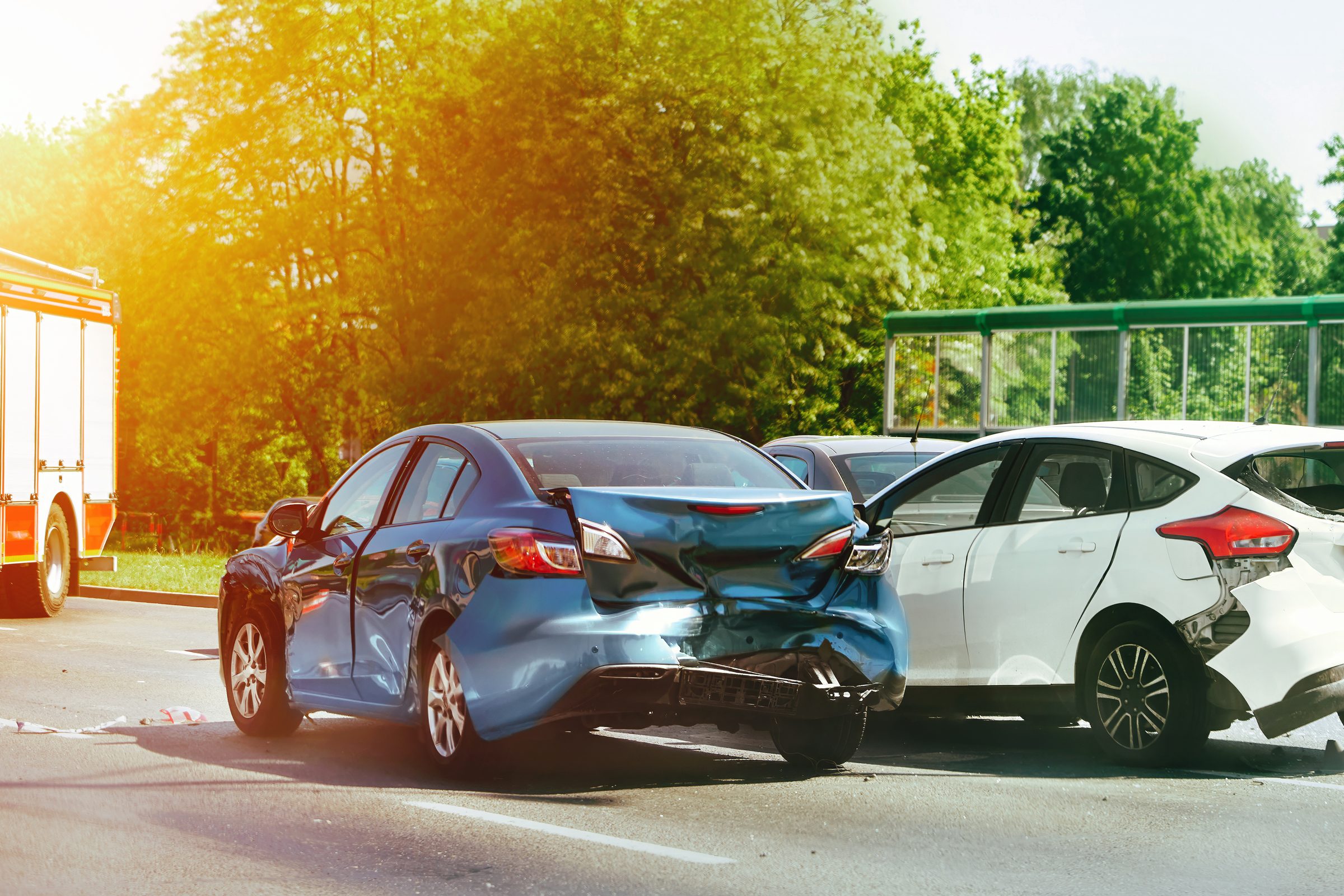 Blue sedan and white car damaged in a collision, with a fire truck on scene