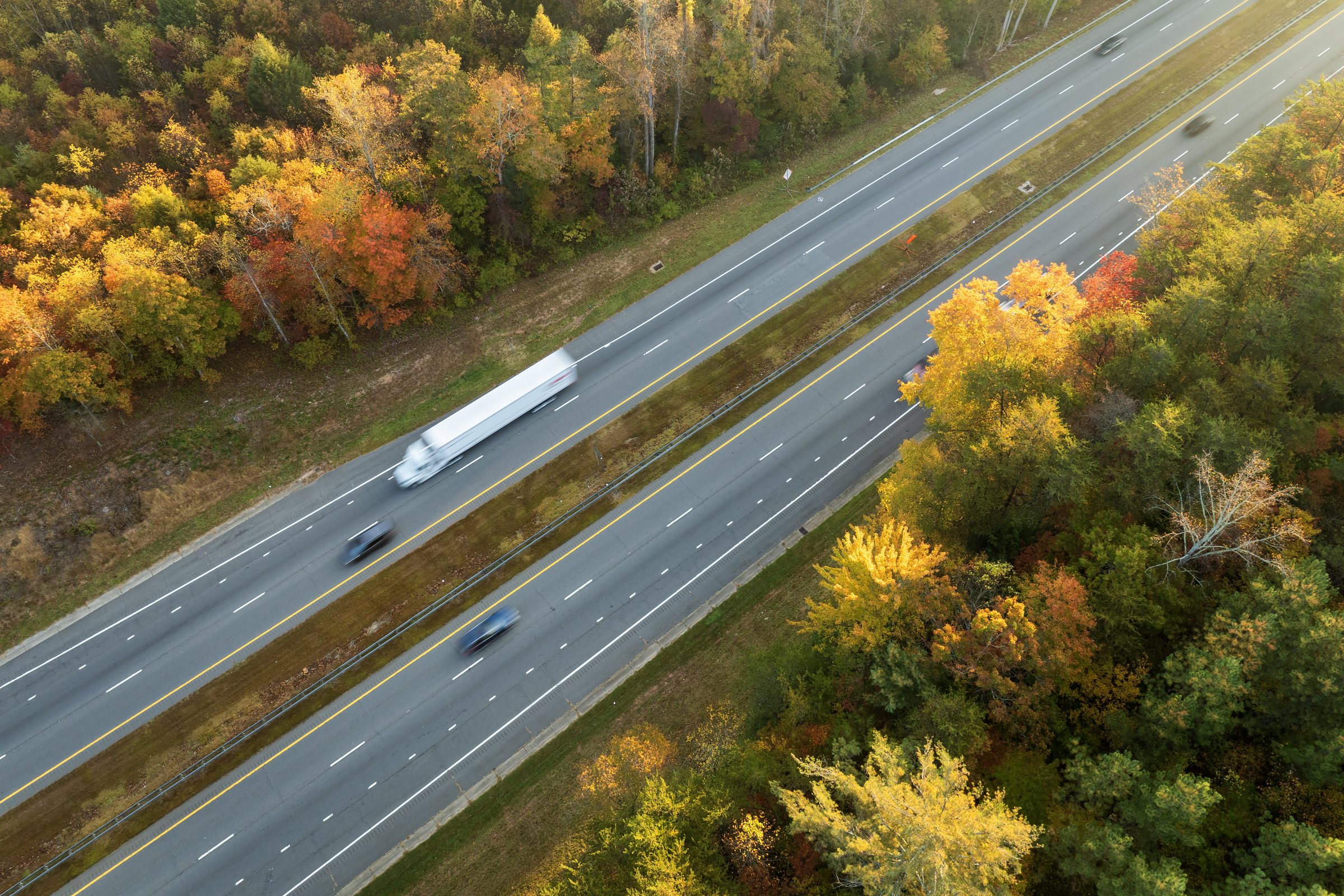 Semi-truck on a four-lane interstate through fall-colored Appalachian hills, seen from above